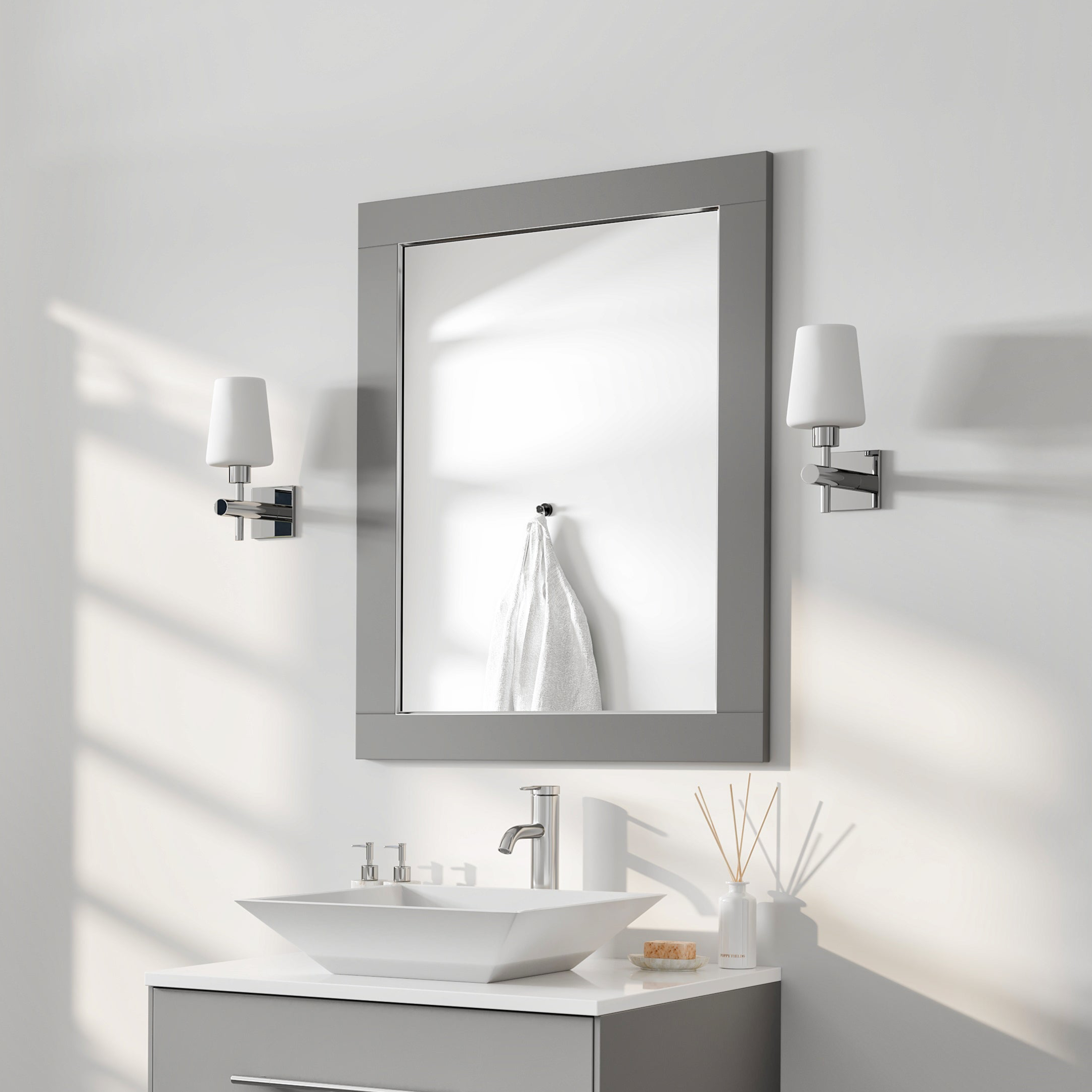 Rectangular gray wooden framed mirror mounted on a wall above a bathroom sink and vanity, with light fixtures on each side.