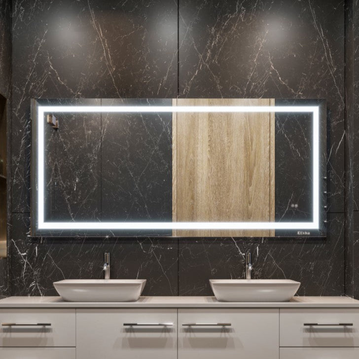 A rectangular, frameless mirror with LED lighting installed above a bathroom vanity with two sinks, set against a dark tiled wall.