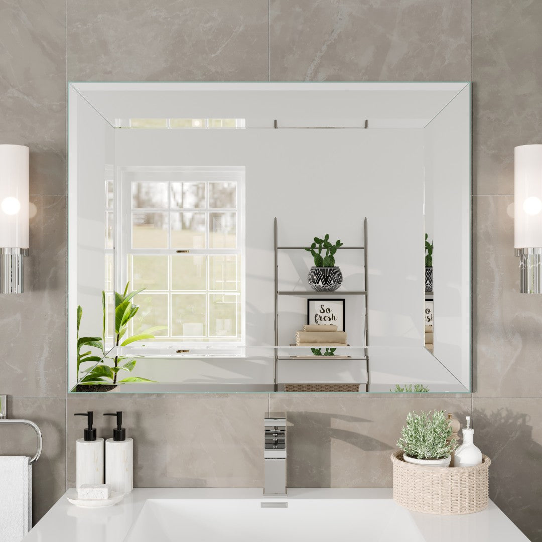 A rectangular frameless mirror mounted on a wall above a bathroom sink, with towels and bathroom accessories displayed.