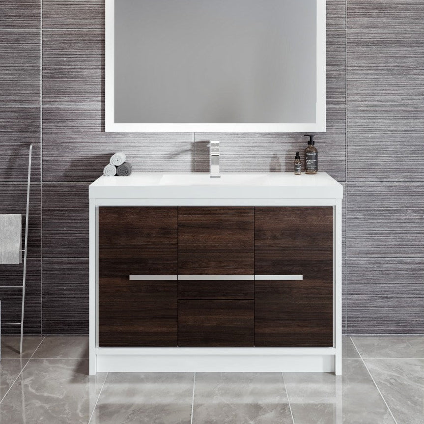 A modern bathroom vanity set which includes a gray oak cabinet with chrome hardware, an acrylic top with an integrated sink, and a rectangular mirror above it, all set against a gray tiled bathroom wall.