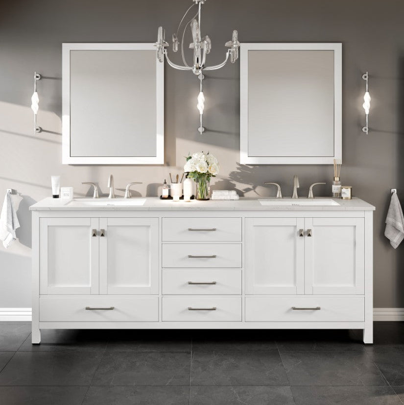 A white double sink bathroom vanity with a Carrara quartz top, undermount porcelain sinks, and gold hardware. The image shows the vanity in a stylish bathroom setting with a chandelier, mirrors, and decorative items.