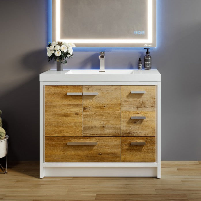 A modern bathroom vanity featuring natural oak wood finish with white, an integrated sink, and chrome hardware. The image shows the vanity with an illuminated mirror above it, placed in a bathroom setting with decorative items and a plant.