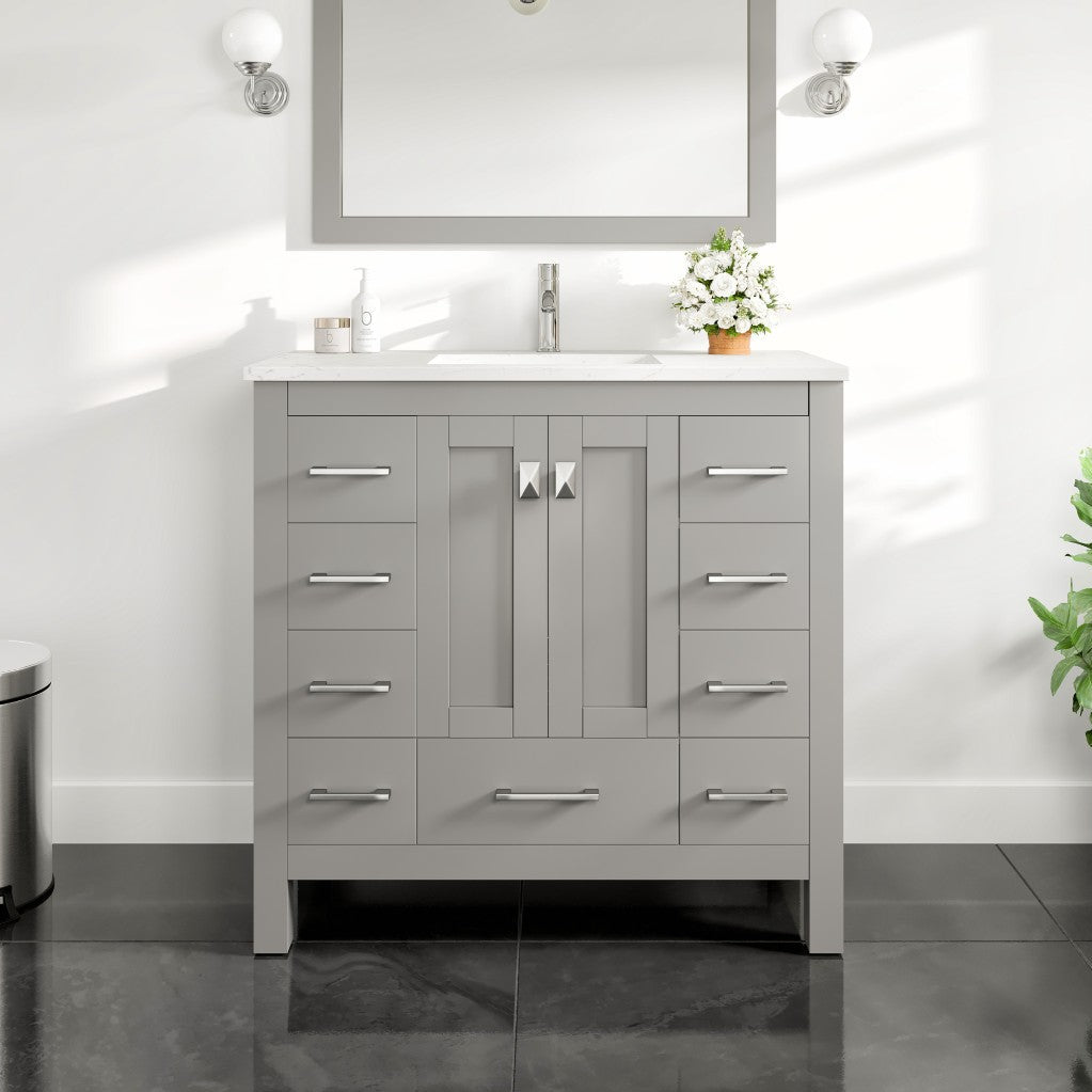 A gray single sink bath vanity with a Carrara quartz top and undermount porcelain sink, displayed in a bathroom setting with necessary accessories like a mirror, lights, and a plant.
