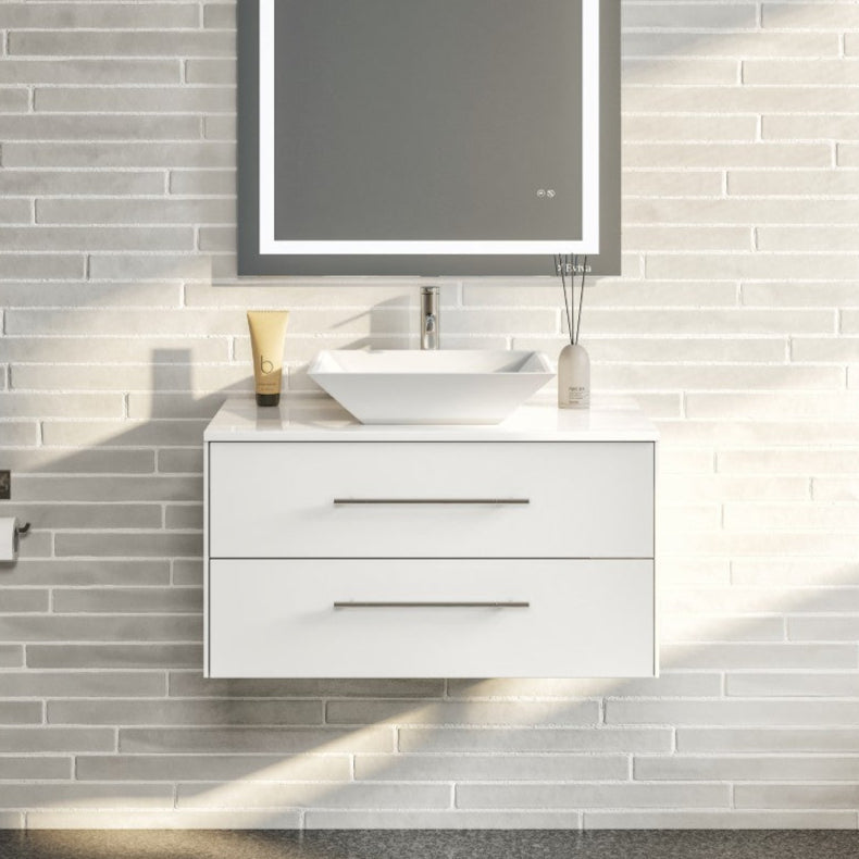 A modern white wall mount single sink bath vanity with a white quartz top and a vessel porcelain sink, mirrored by a rectangular mirror with a built-in light strip.