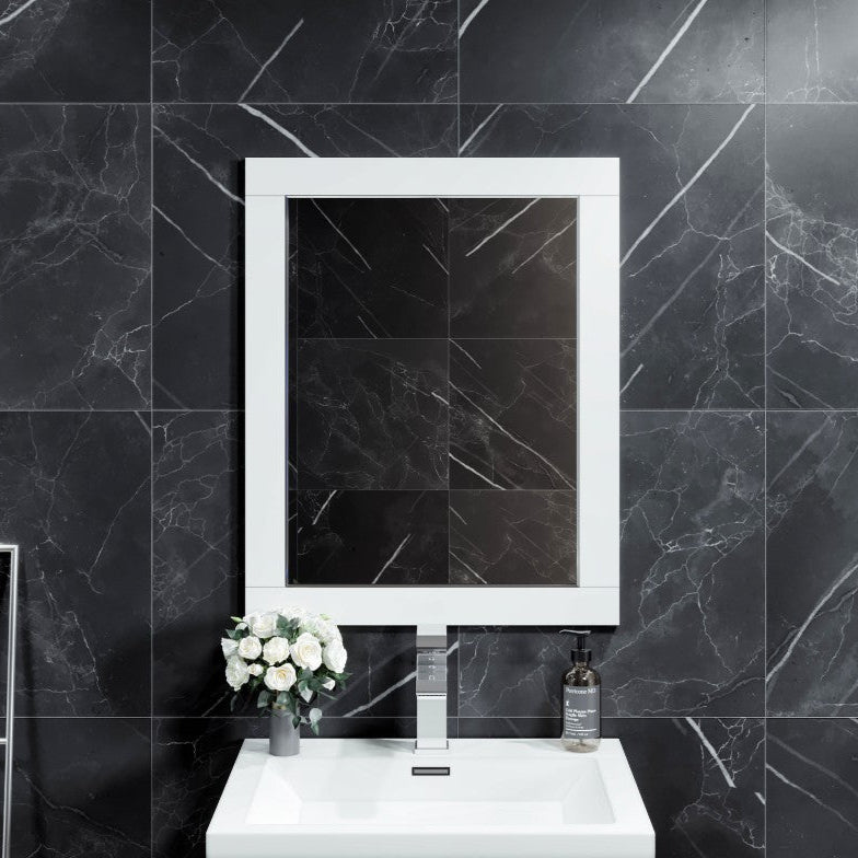 A rectangular white wooden framed mirror mounted on a wall with a black marble tiled wall in the background, placed above a white sink.