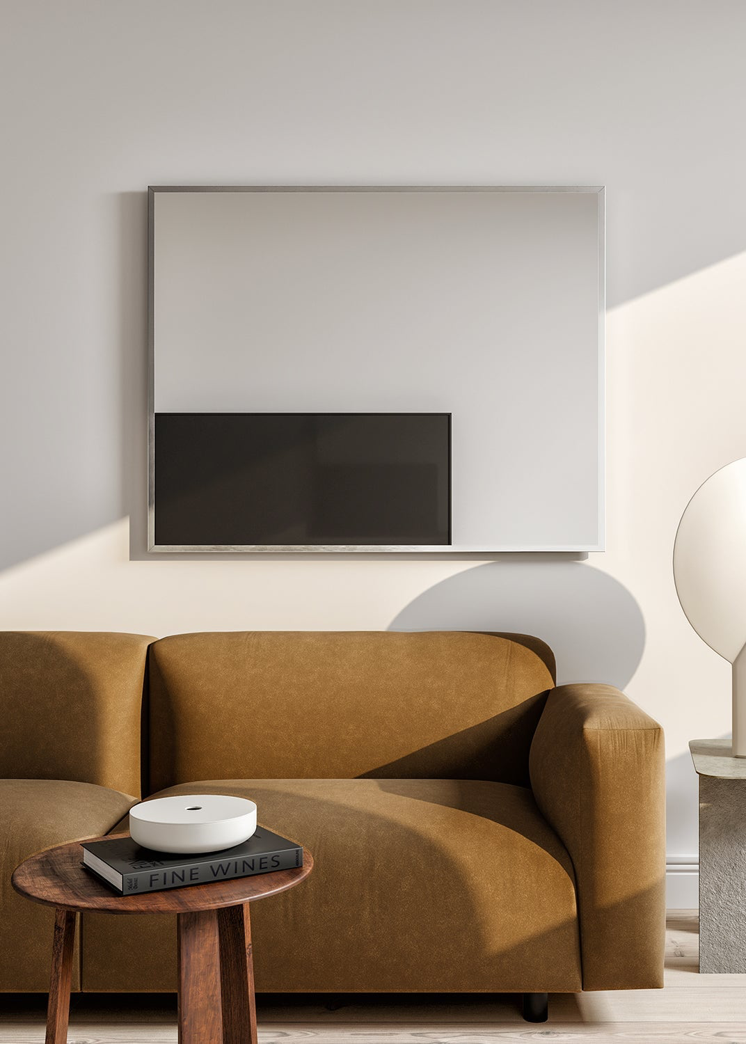 A brown sofa in front of a wall-mounted rectangular mirror and a stack of books on a table