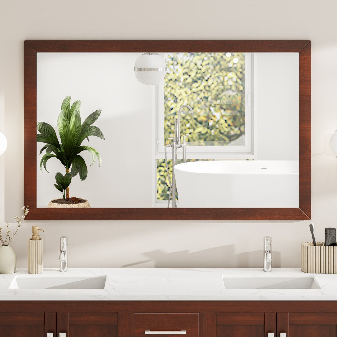 A rectangular brown wooden framed mirror mounted above a bathroom sink, with a burst of greenery visible through the reflection.