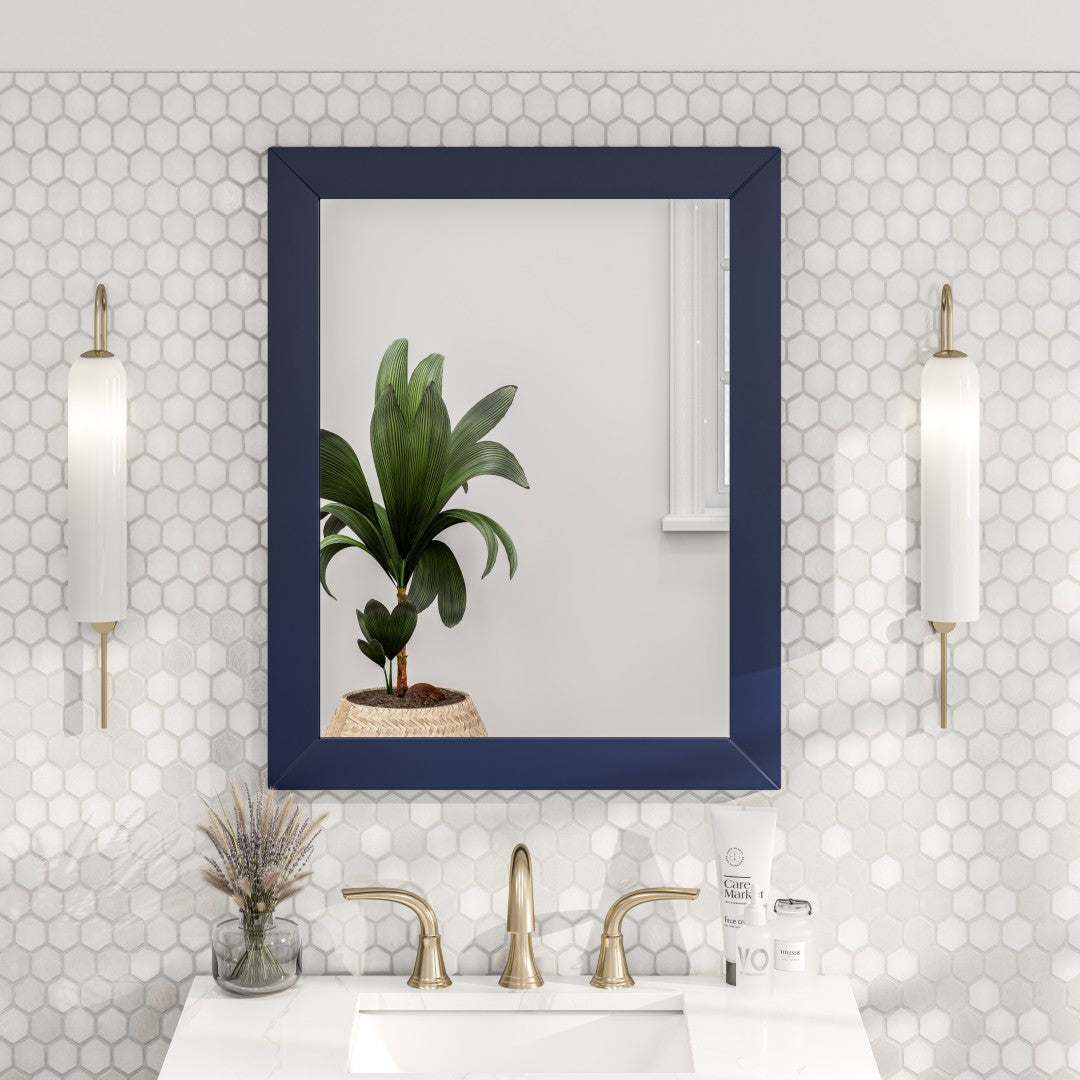 A dark blue framed mirror hanging on a light-colored wall with scone lights on the side and vanity
