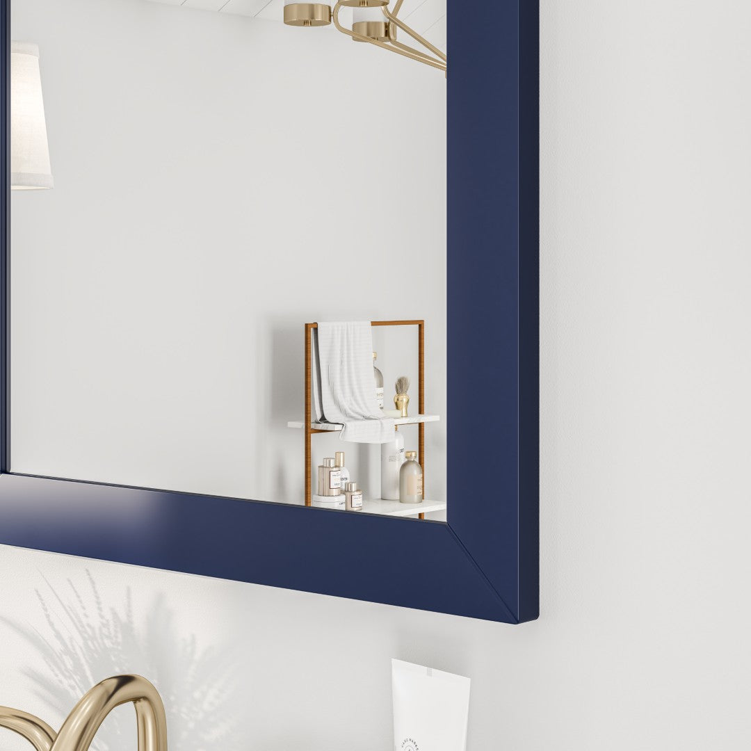 Edge of a dark blue framed mirror hanging on a light-colored wall with bath essentials