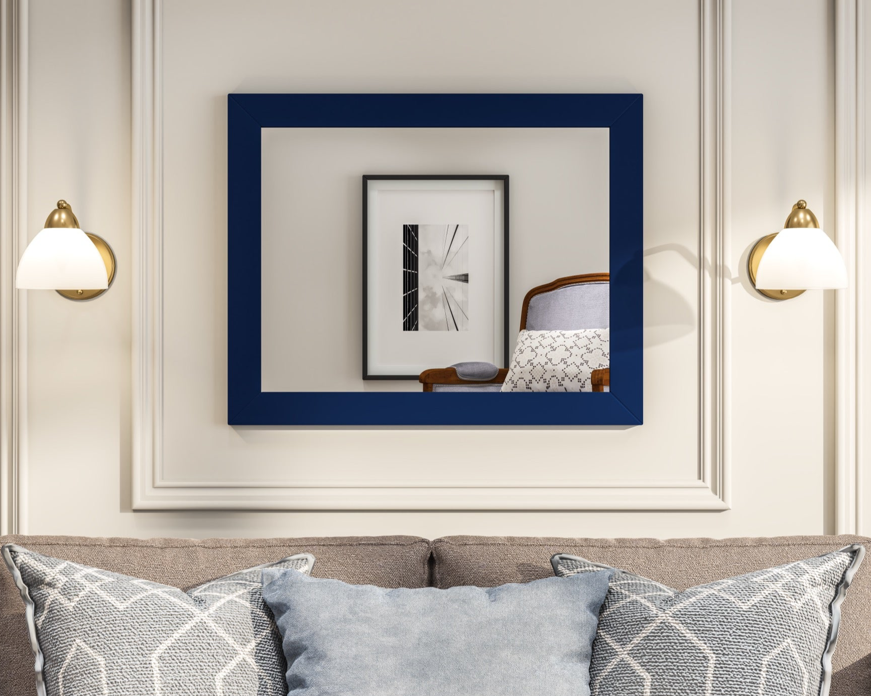 A square, dark blue framed mirror hangs on a light-colored wall above a couch with patterned pillows showing two sconce lights on both side
