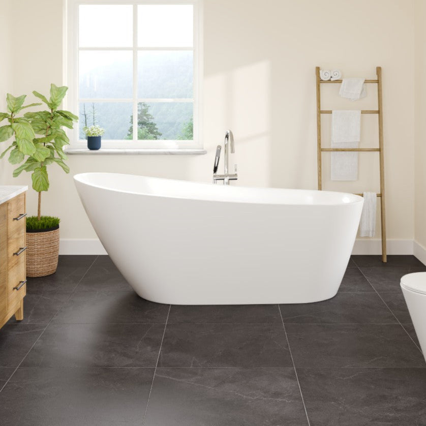 A glossy white acrylic slipper freestanding bathtub positioned in a room with a window, alongside a wooden cabinet and a plant.