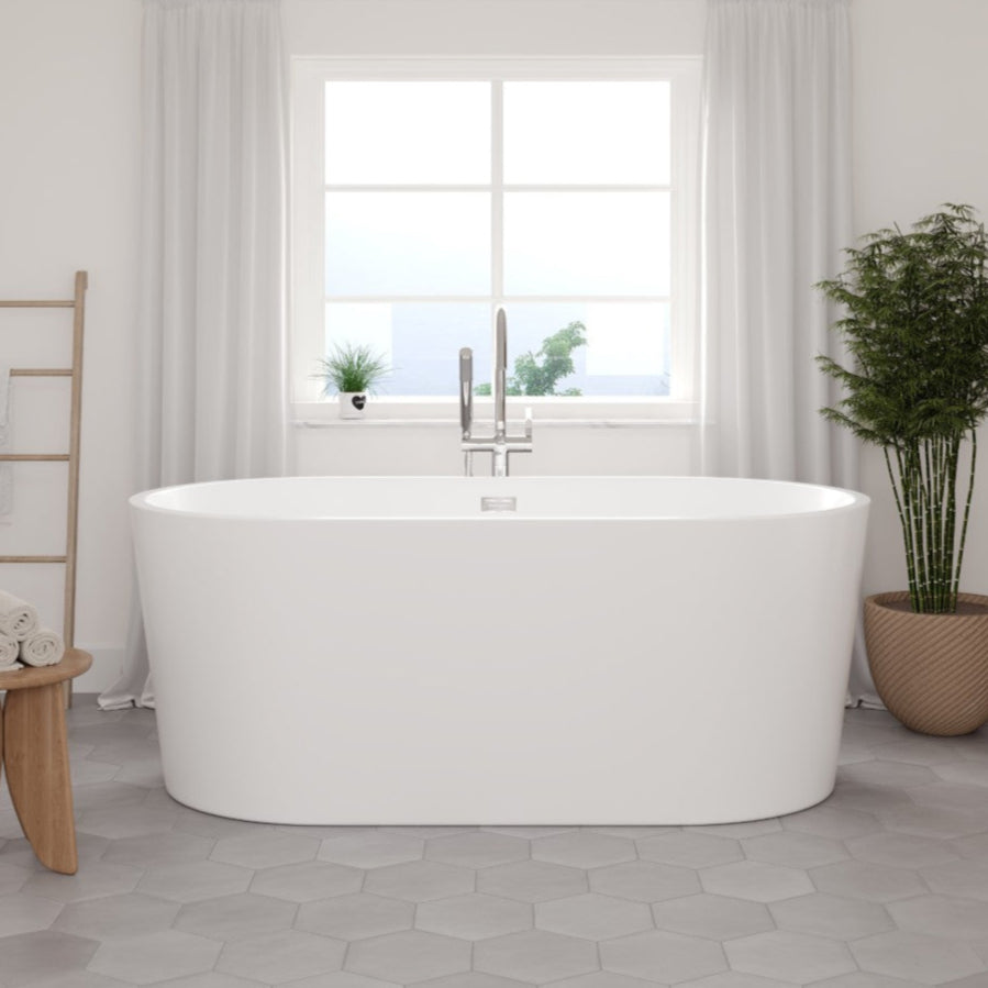 A glossy white acrylic oval freestanding bathtub placed in a bathroom setting with light-colored tiles on the floor, a window in the background, and a potted plant to the side.