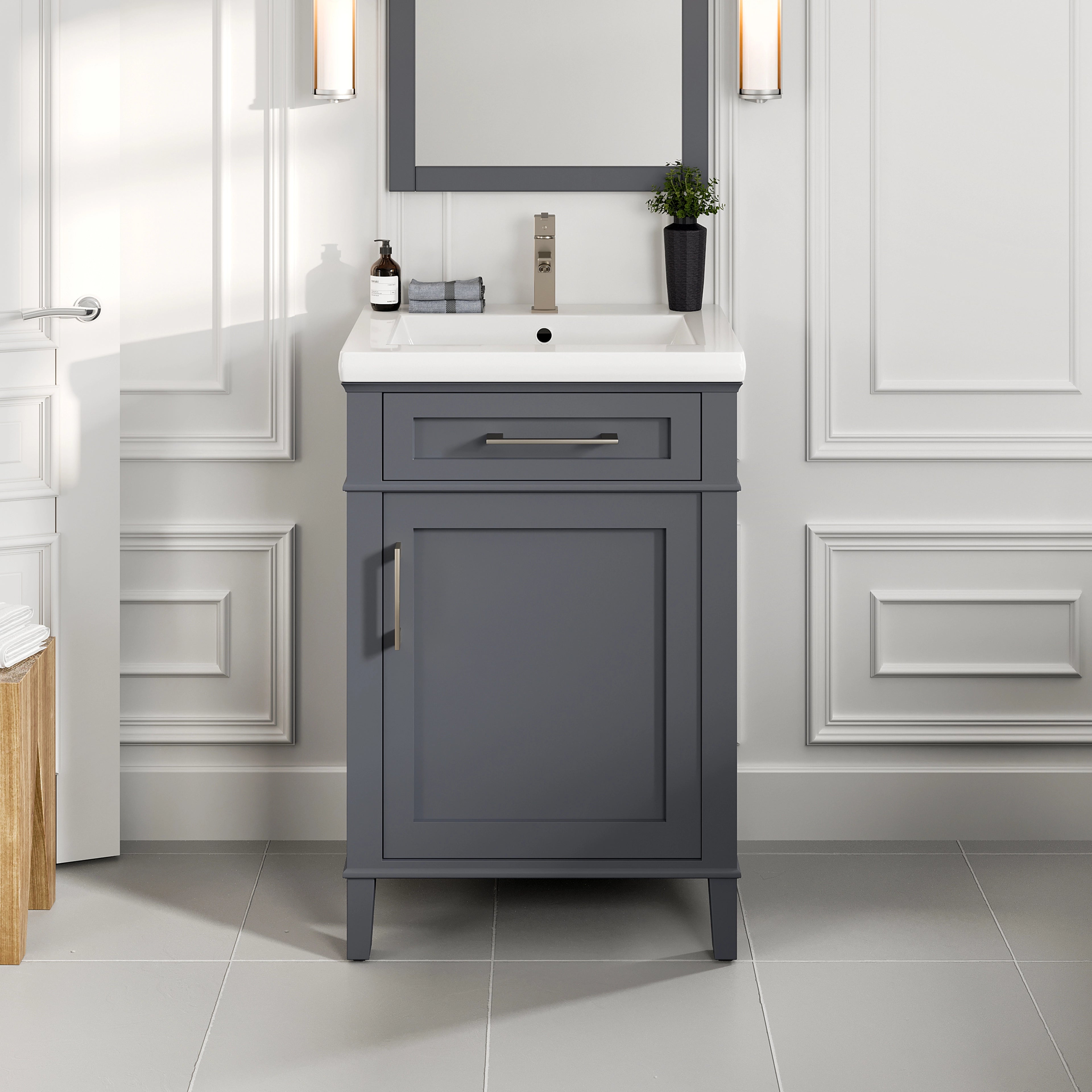 A dark gray single sink bath vanity with a porcelain top and integrated sink, featuring a soft closing door and premium stainless steel brushed nickel hardware, set against a bathroom backdrop with light colored walls and a mirror.