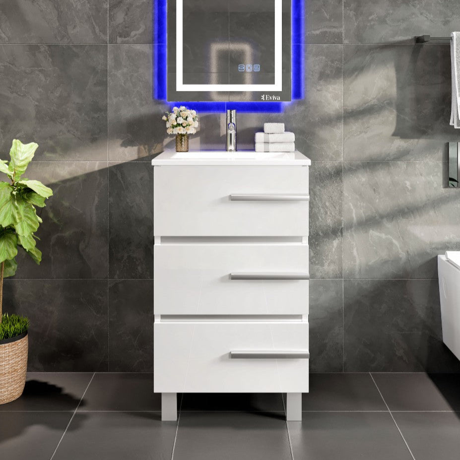 A white single sink bath vanity with three drawers, an integrated sink, and chrome hardware, placed in a bathroom setting with a plant and a mirror in the background.