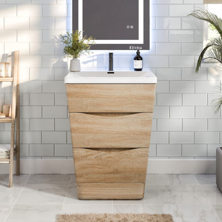 A white oak single sink bath vanity with an acrylic top and integrated sink, displayed in a bathroom setting with a mirror above it, plants and bathroom accessories in the background.