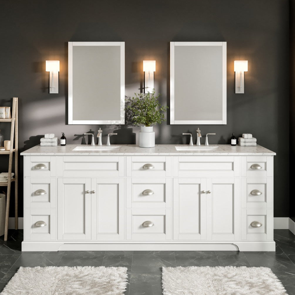 A white double sink bathroom vanity with a Carrara quartz top, undermount porcelain sinks, and silver handles. The vanity is placed against a dark wall with two mirrors and sconces above it.