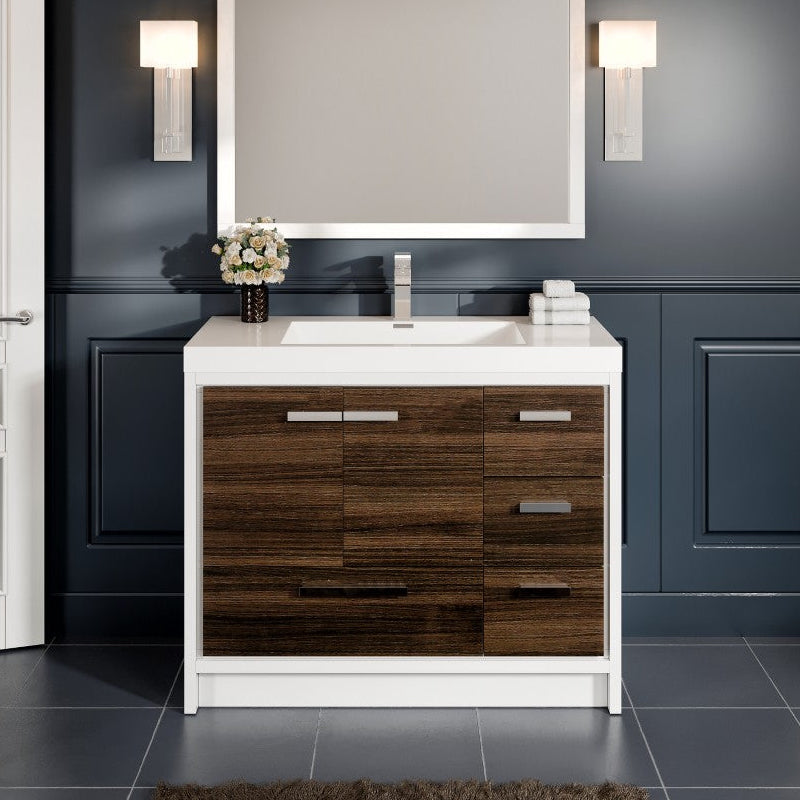 A modern bathroom vanity with gray oak finish and white acrylic countertop, featuring soft-closing drawers and chrome hardware, with a mirror above the sink and wall sconces on either side.