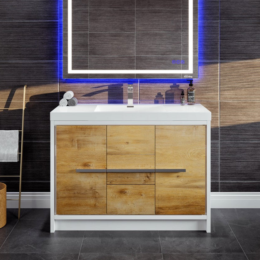 A modern bathroom vanity featuring a natural oak finish with a white acrylic countertop, integrated sink, and chrome hardware. The image showcases the vanity in a bathroom setting with a illuminated mirror above it.