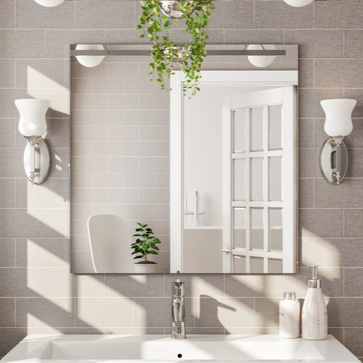 A modern elegance frameless mirror with beveled edges mounted above a bathroom sink and vanity, with light fixtures on either side.