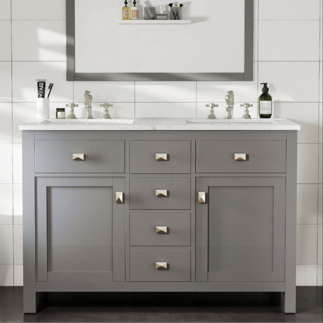 A gray double sink bathroom vanity with undermount porcelain sinks and stainless steel hardware, against a white tile wall.