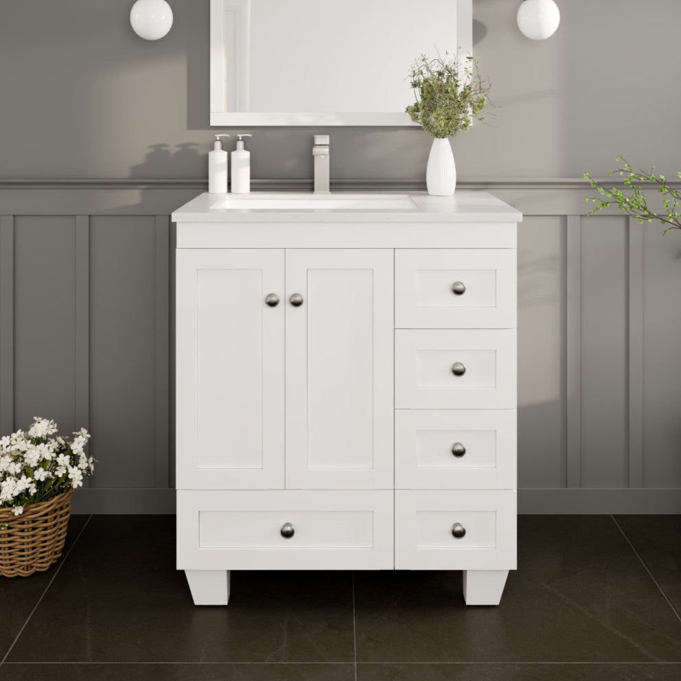 A white single sink bath vanity with a Carrara quartz top and undermount porcelain sink, featuring a white finish, wooden drawers, and stainless steel hardware, placed against a gray wall with dark flooring.