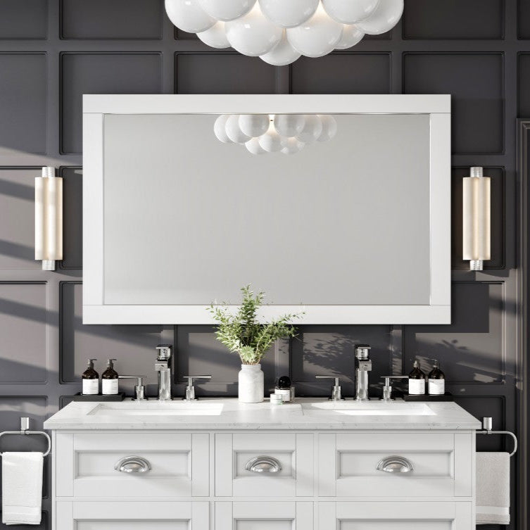 A white wooden framed mirror with beveled edges, mounted on a bathroom wall above a vanity.