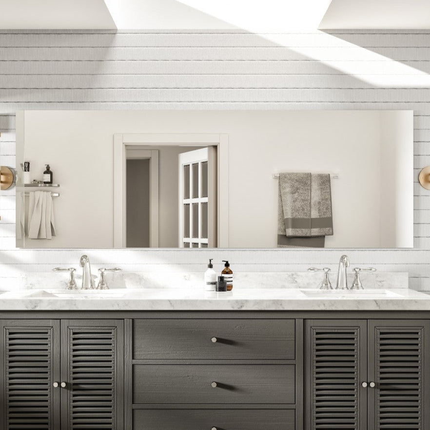 A rectangular, frameless mirror with beveled edges mounted on a bathroom wall above a vanity with two sinks.