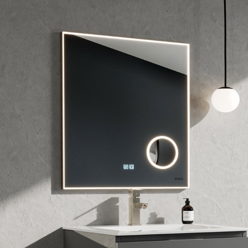 Modern square LED mirror with chrome aluminum frame, featuring a round magnifier circle, mounted on a grey wall above a white sink and grey vanity.
