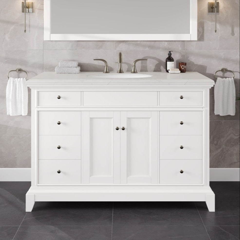 A white single sink bath vanity with a Carrara quartz top and undermount porcelain sink, featuring a traditional design with multiple storage drawers and a mirror above.